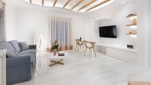 Un salón moderno con un sofá gris, una mesa de centro redonda, una zona de comedor con mesa y sillas, un televisor montado en la pared y una estructura de techo de madera.