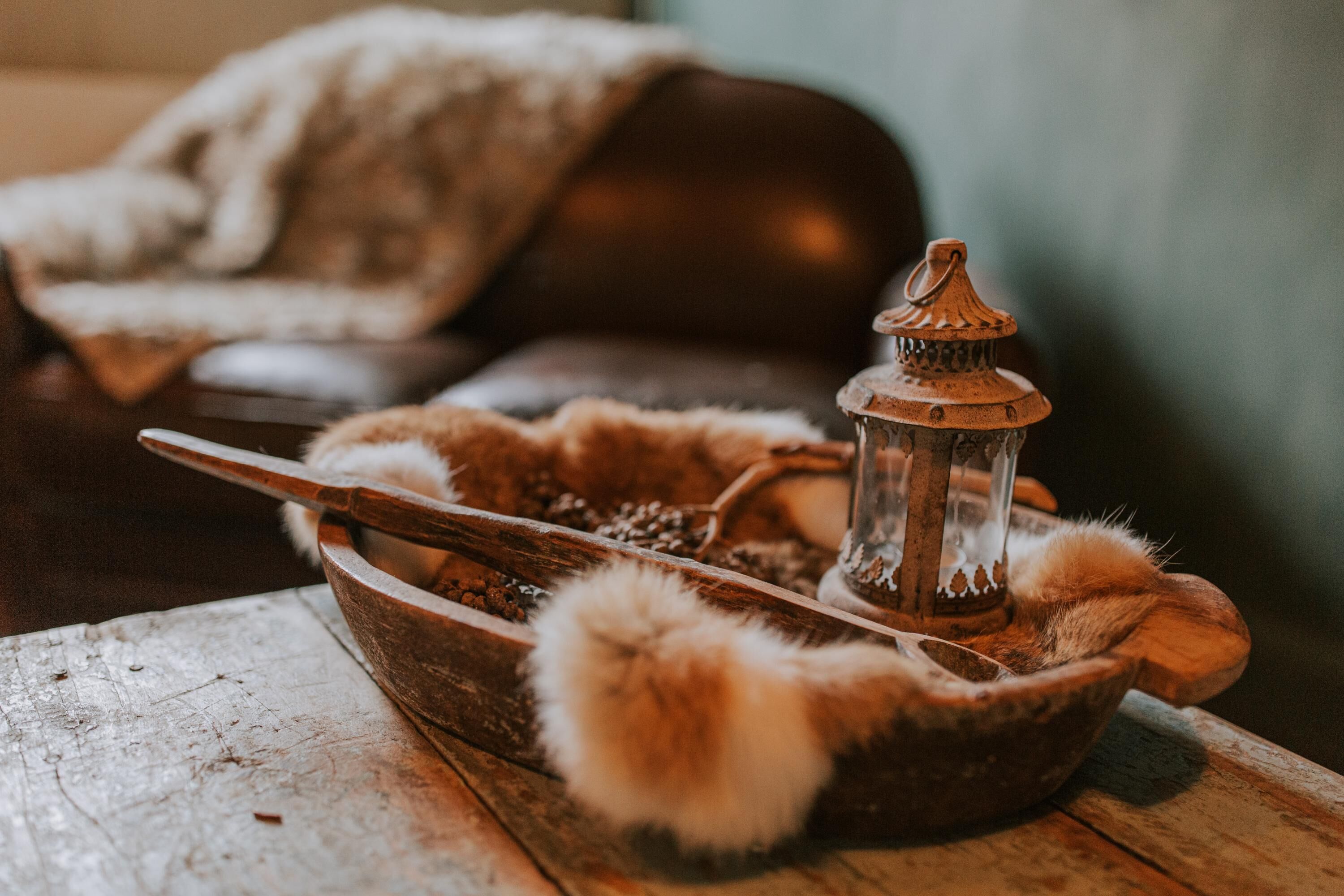 A rustic wooden bowl with a spoon and a lantern, surrounded by fluffy white material.