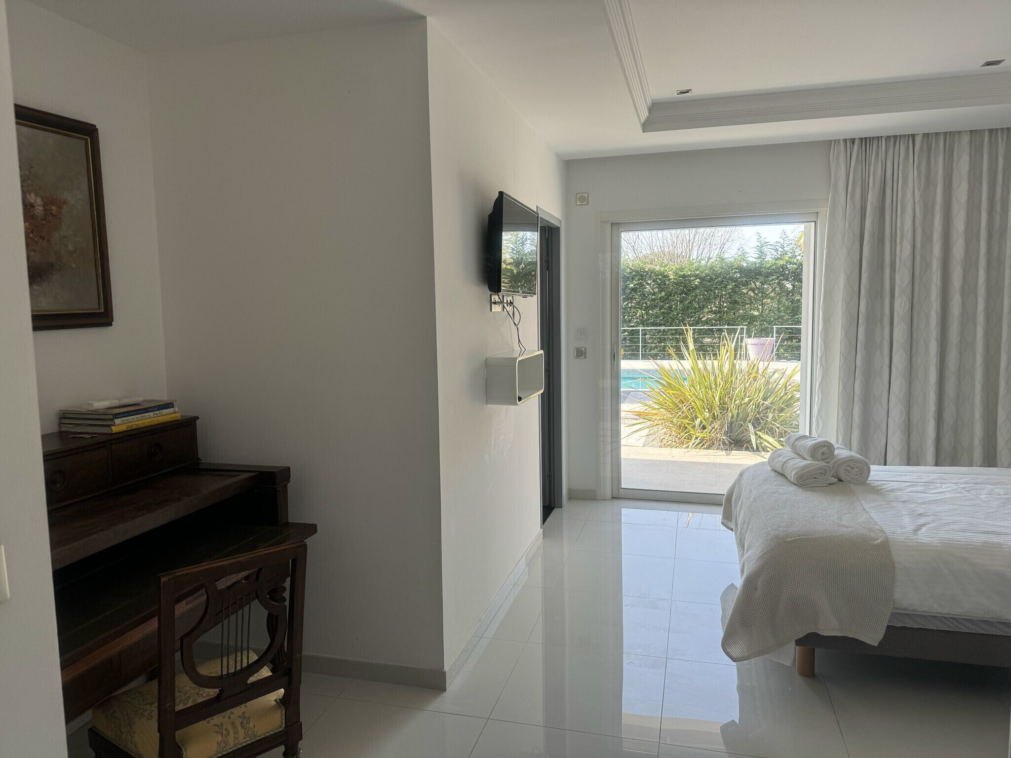 Ein Hotelzimmer mit einem Bett, einem Schreibtisch mit Büchern, einem Sessel, einem Fernseher an der Wand und Blick auf einen Pool und Grünflächen.