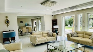 A spacious living room with a glass coffee table, beige sofas, and a dining area with a table and chairs. - Villa Monte-christo - Propriété D'exception au Coeur de la Cote D'azur (Saint-Cézaire-sur-Siagne)
