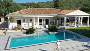 A large swimming pool with a white building in the background, surrounded by greenery and a clear sky. - Villa Monte-christo - Propriété D'exception au Coeur de la Cote D'azur (Saint-Cézaire-sur-Siagne)