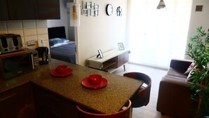 A modern kitchen with a dining area, a bed, and a living room with a sofa and a plant. - Tranquilo Departamento Full Equipado (Santiago)