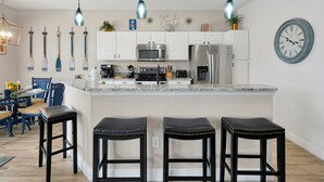 Una cocina moderna con armarios blancos, electrodomésticos de acero inoxidable y una isla central con taburetes de bar.