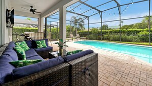 Un espacio al aire libre cubierto con piscina, mobiliario de mimbre y ventilador de techo.