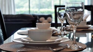 Mesa de comedor preparada con cuencos, platos y una copa de vino, con vista a follaje a través de la ventana.