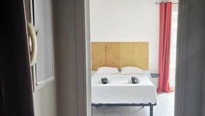 Una habitación con una cama, cabecera y cortina roja.