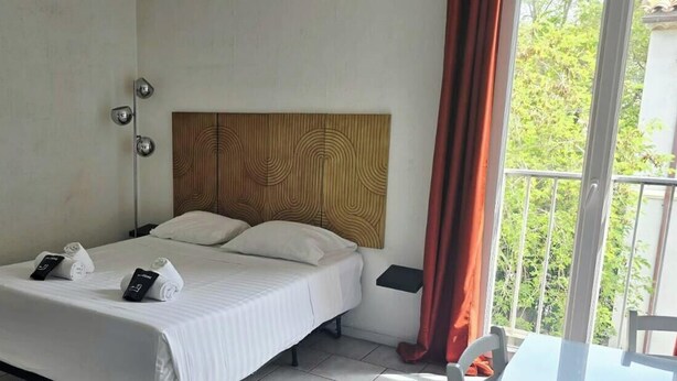 Habitación de hotel con cama, mesita de noche, cortinas y vista a zonas verdes.