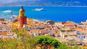 Un pueblo costero con una imponente torre del reloj, una extensa masa de agua y un crucero al fondo.
