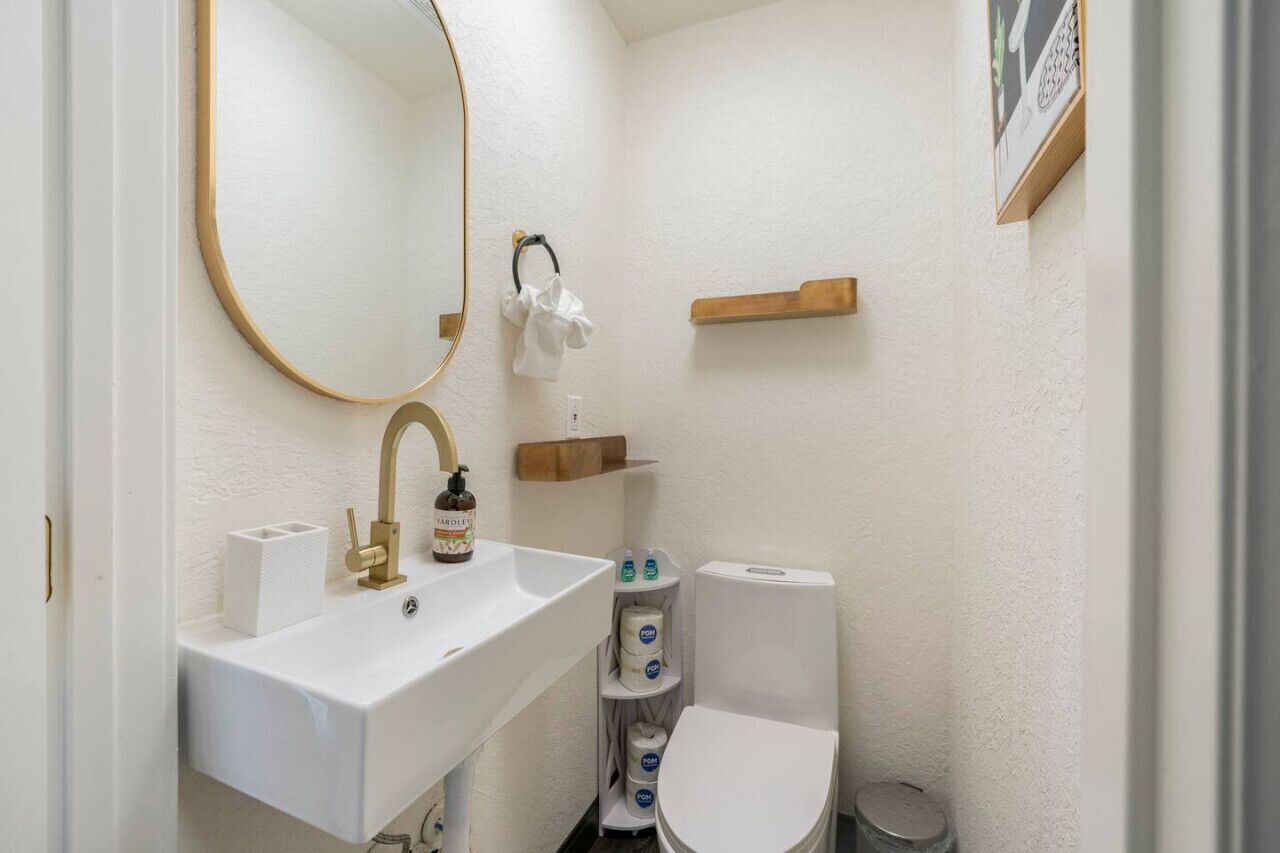 Un bagno piccolo e compatto con lavandino bianco, uno specchio, un water e uno scaffale con articoli da toilette.
