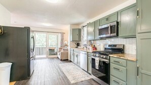 Une cuisine avec un plancher en bois foncé, des armoires vertes, un réfrigérateur en acier inoxydable, un four à micro-ondes et une cuisinière.