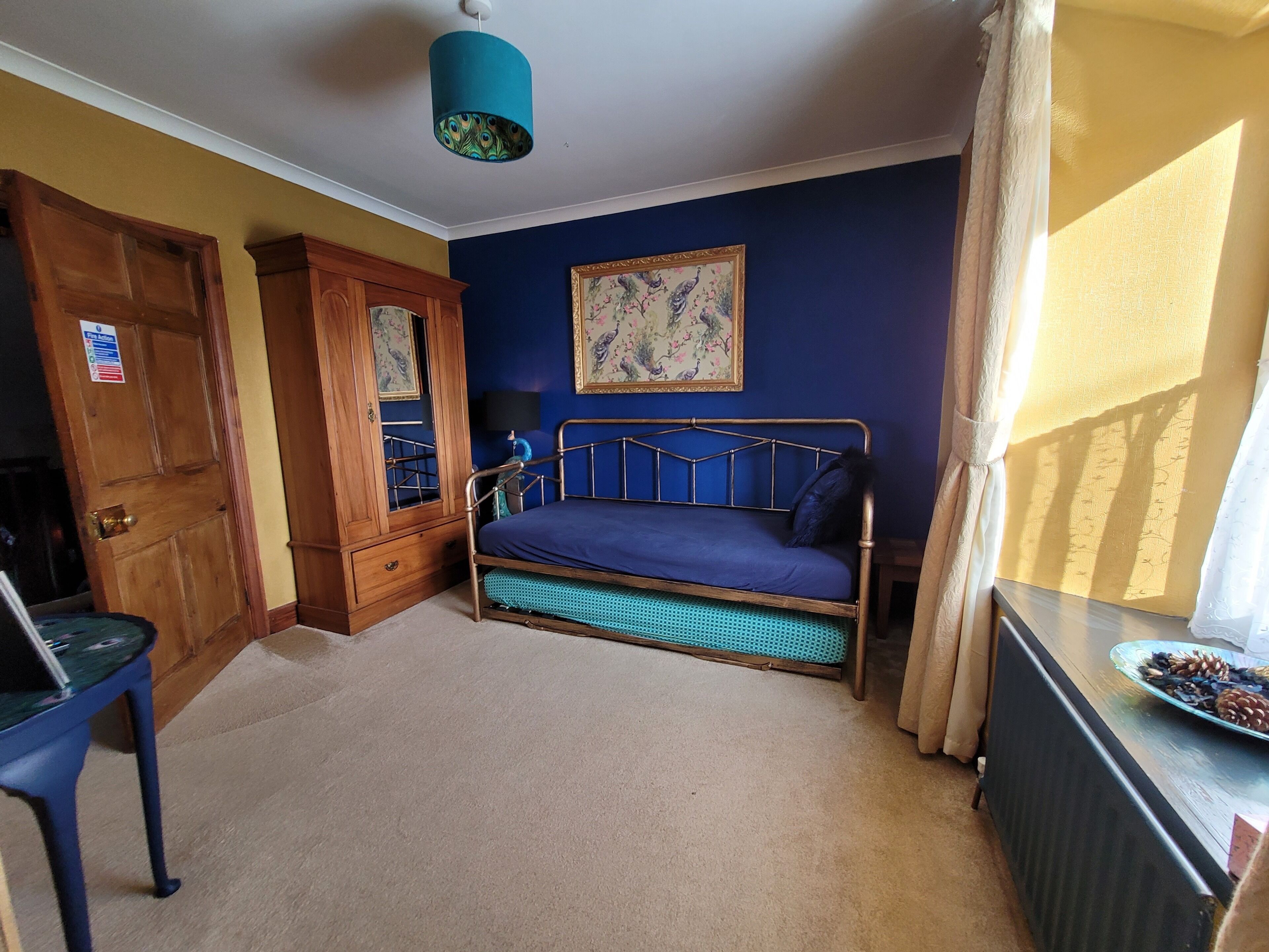 A bedroom with a bed, a wooden wardrobe, a blue wall, and a window with curtains.