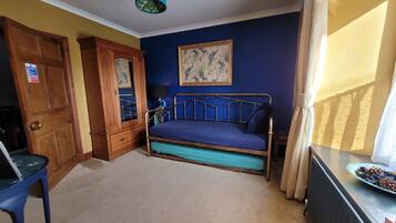 A bedroom with a bed, a wooden wardrobe, a blue wall, and a window with curtains.