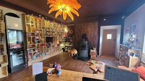 Ein gemütliches Zimmer mit Holzboden, einer großen Bücherwand voller Bücher und Dekoration, einem Kamin und einer Essecke mit Tisch und Stühlen.
