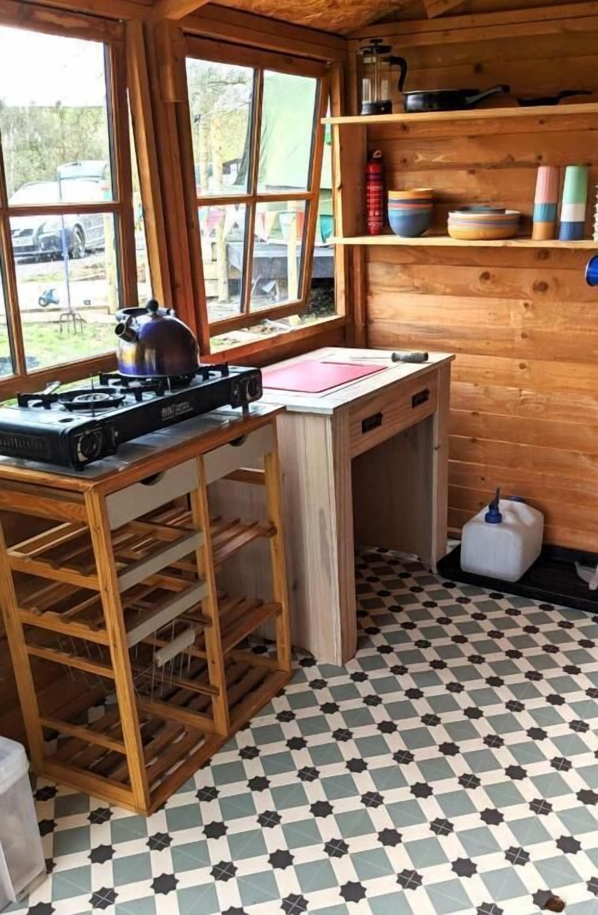A kitchen with a gas stove, wooden shelves, and a checkered floor.