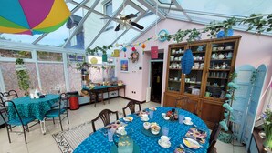 Ein Wintergarten mit Essbereich, dekoriert für eine Gartenparty, mit Tisch, blauem Tischläufer, Stühlen und verschiedenen Geschirrteilen.
