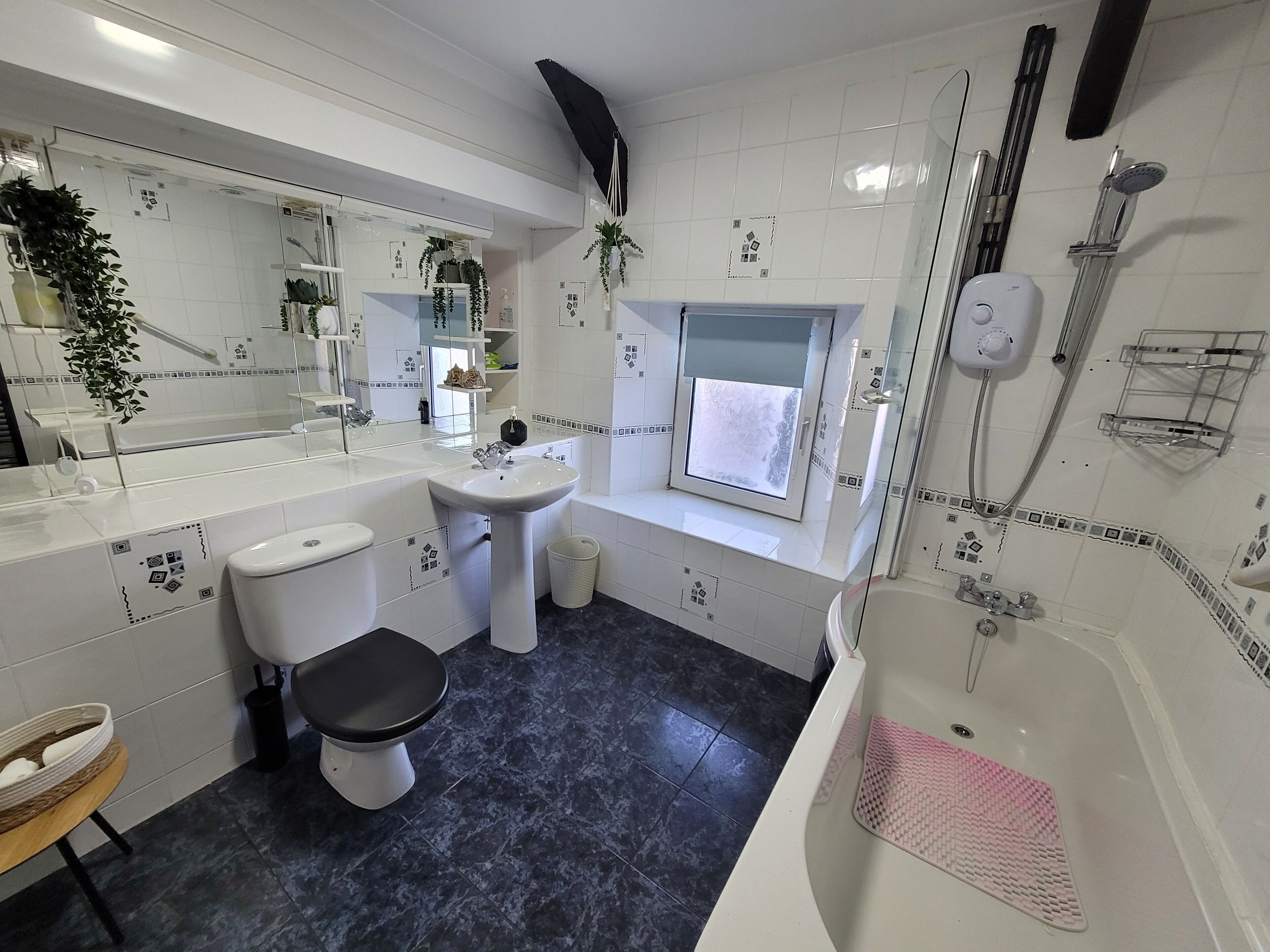 A modern bathroom with a white sink, toilet, and bathtub. There is a window above the bathtub, a showerhead, and a towel rack.