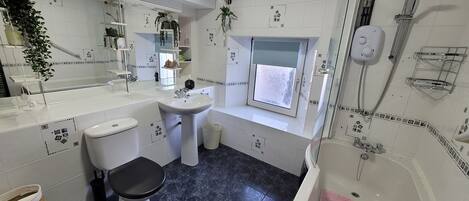 A modern bathroom with a white sink, toilet, and bathtub. There is a window above the bathtub, a showerhead, and a towel rack.