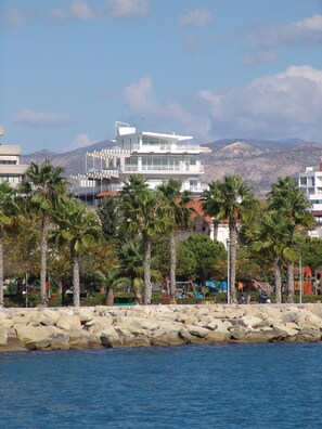 A coastal building with a modern design, surrounded by palm trees and a rocky shoreline. - 1-80 Collection Apt 301 (Limassol)
