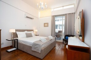 Habitación de hotel con una cama grande, mesitas de noche, un escritorio, una silla, un espejo y vistas al exterior a través de una ventana.
