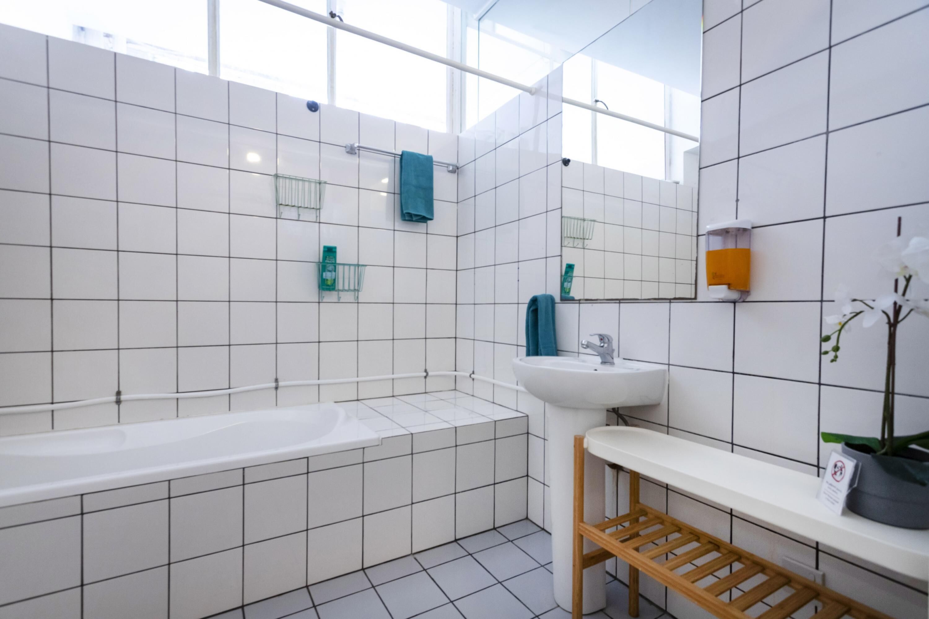 Ein modernes Badezimmer mit Badewanne, Waschbecken und Spiegel. Es gibt grüne Seifenspender und einen Handtuchhalter.