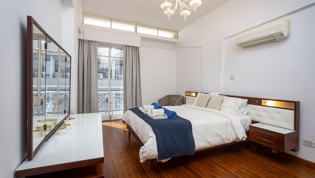 A hotel room with a large bed, a bedside table, a mirror, and a window with curtains. - 1-80 Collection Apt 202 (Limassol)