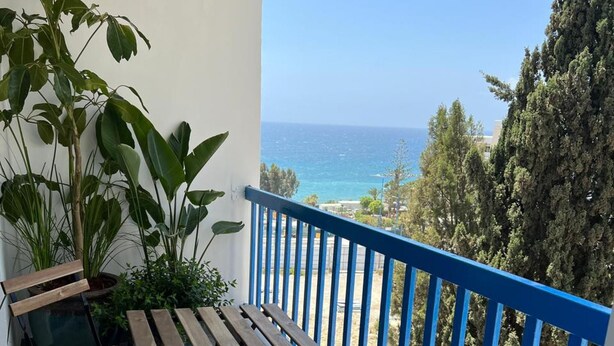 A balcony with a blue railing, a wooden table, and chairs, overlooking a coastal view. - White Arches Sea View Apt No 2 (Limassol)