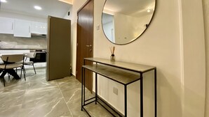 A modern kitchen with white cabinets, a dining area with chairs, and a console table with a mirror and reed diffuser. - White Arches Sea View Apt No 2 (Limassol)