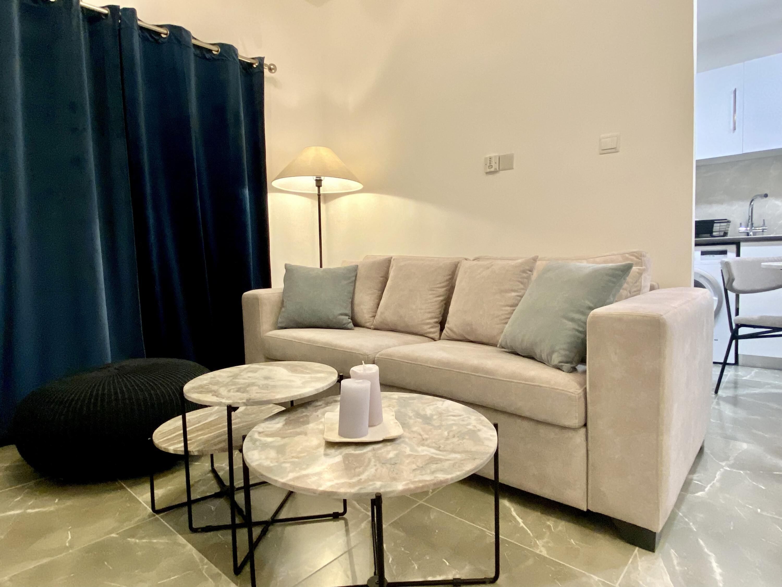 A living room with a sofa, two round tables, a lamp, and a blue curtain.