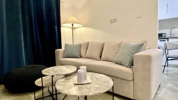 A living room with a sofa, two round tables, a lamp, and a blue curtain.