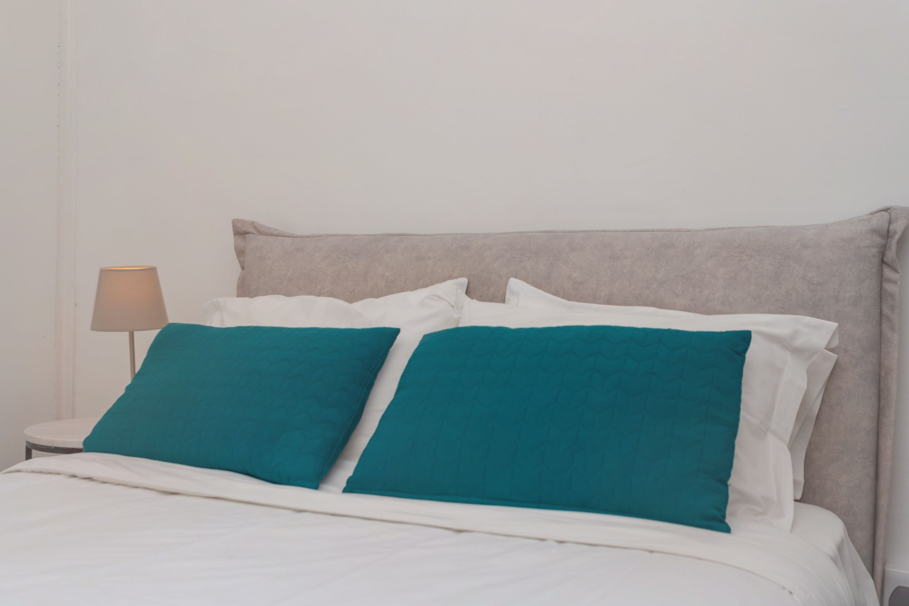 Una cama con ropa de cama blanca y dos almohadas color turquesa.