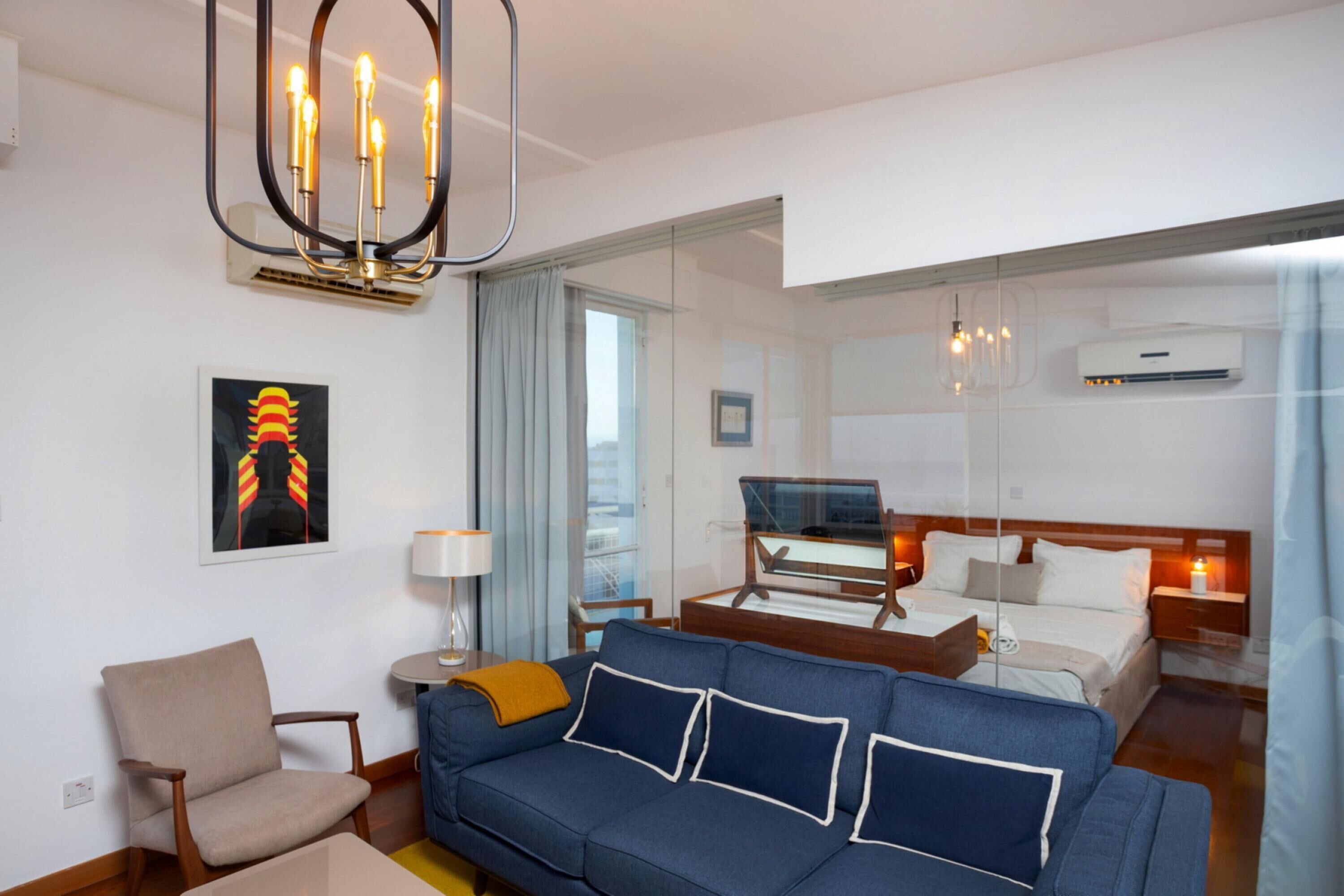 Een moderne hotelkamer met een blauwe bank, een houten bijzettafeltje, een lamp en een bed met een houten hoofdeinde.