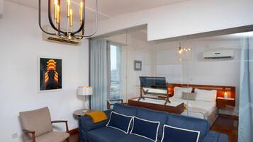 Een moderne hotelkamer met een blauwe bank, een houten bijzettafeltje, een lamp en een bed met een houten hoofdeinde.
