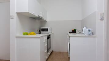 A compact kitchen with white cabinetry, a microwave, a toaster, and a small countertop with fruits.