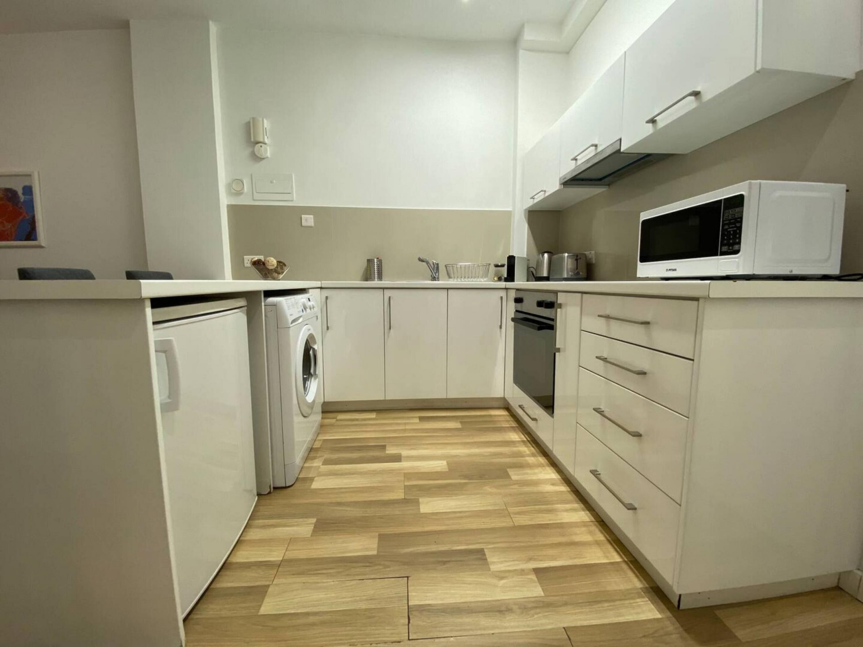 A compact kitchen with white cabinets, a built-in washing machine, a microwave, and a stove.
