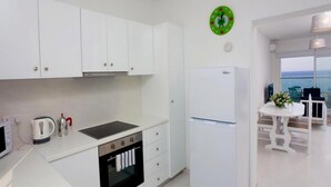 A modern kitchen with white cabinets, a built-in oven, a refrigerator, and a view of the sea through large windows. - On the Beach Penthouse (Limassol)