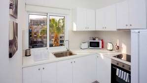 A modern kitchen with white cabinets, a stainless steel sink, a microwave, a toaster, and a refrigerator. - On the Beach Penthouse (Limassol)