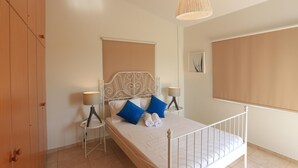 A neatly made bed with blue pillows, a white headboard, and two bedside lamps. - Seabreeze Villa No 4 (Sotira)