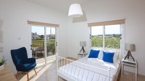 A bedroom with a bed, a chair, a balcony, and a view of the outside. - Seabreeze Villa No 4 (Sotira)
