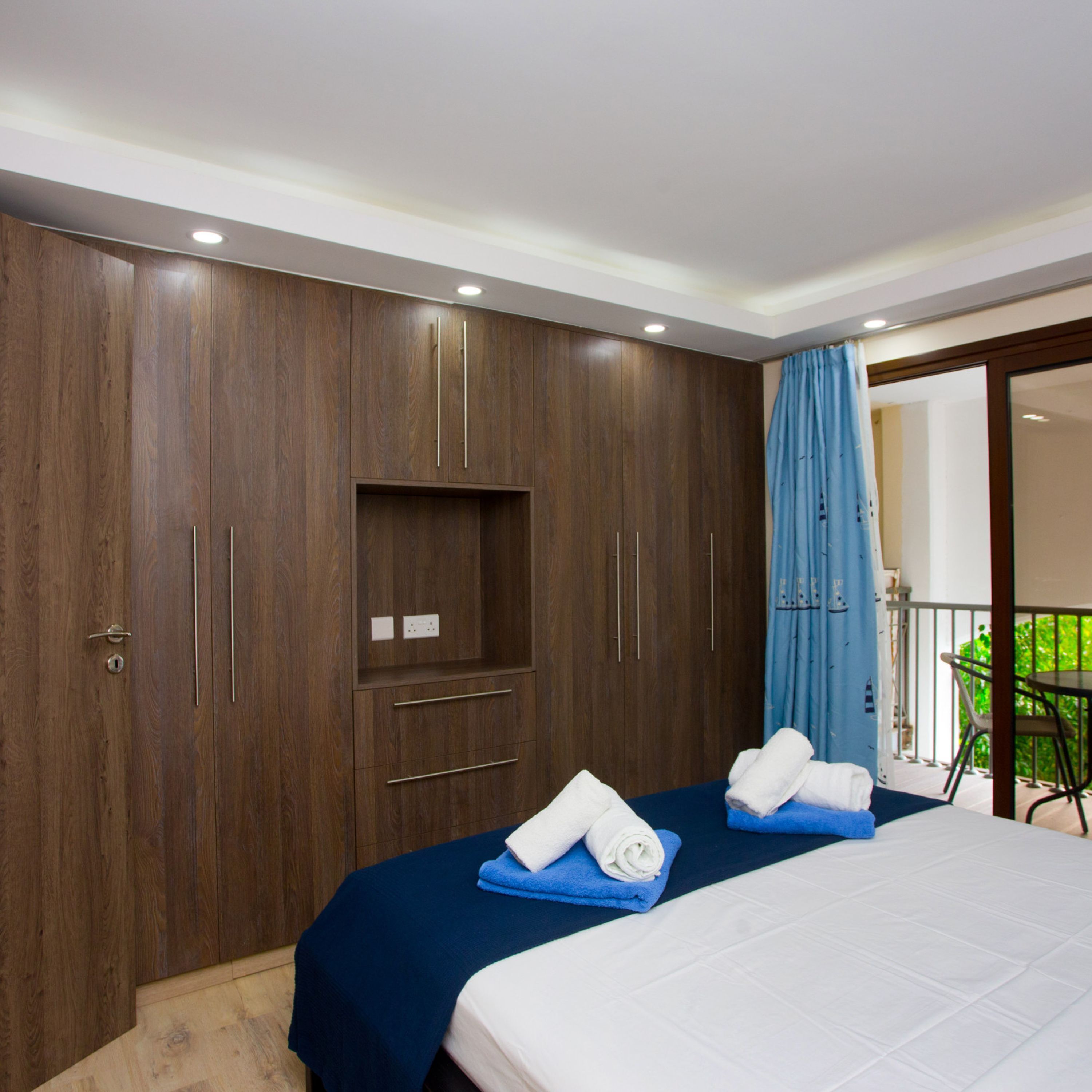 Een hotelkamer met een ruime kast, een bed met blauw-witte lakens en een balkon met een stoel en een tafel.