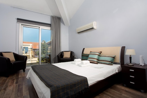 A hotel room with a large bed, a chair, a nightstand, and a window with a view of buildings and greenery.