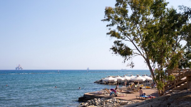 Una spiaggia con un litorale roccioso, ombrelloni e persone che si rilassano.