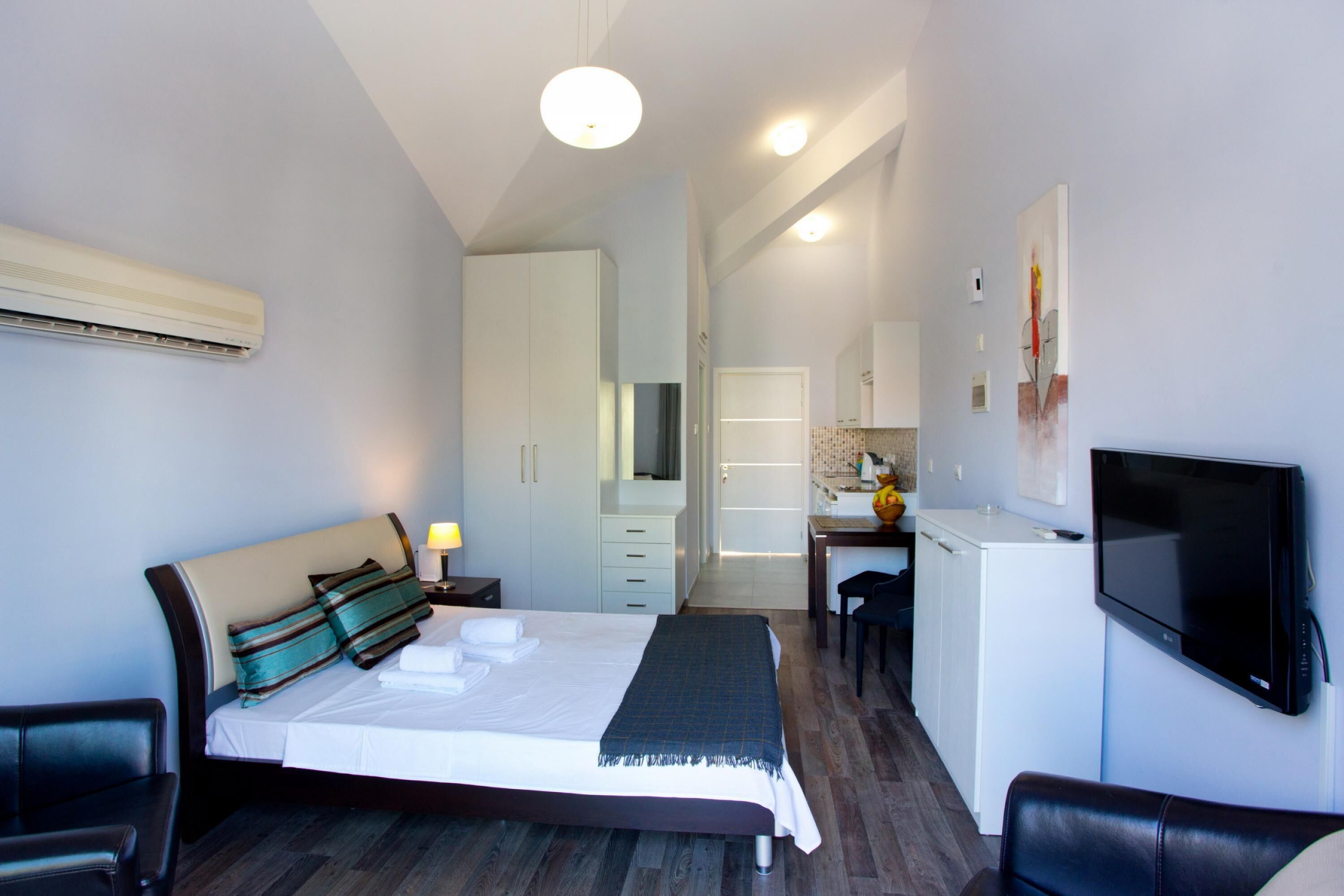Een moderne hotelkamer met een bed, een bureau, een televisie en een kitchenette.
