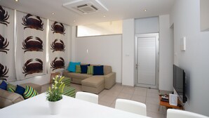 Uma sala de estar moderna com um sofá bege, uma mesa de jantar e uma televisão em um suporte.