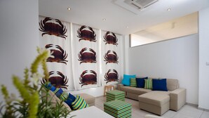 Uma sala de estar moderna com um sofá bege, pufes listrados e uma parede grande com impressões de caranguejos.