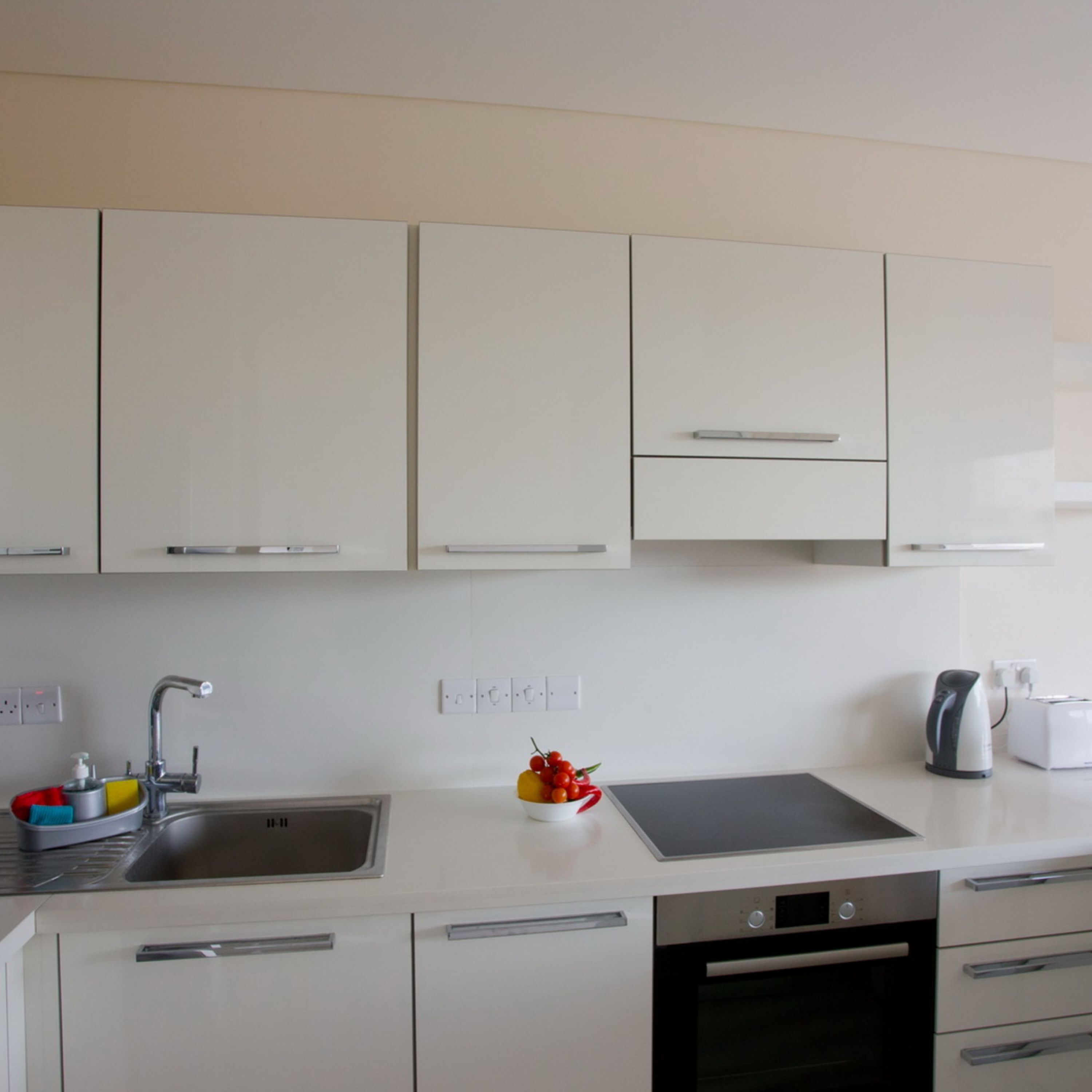 Una cocina moderna con armarios blancos, un lavamanos de acero inoxidable, una tetera y un tostador.