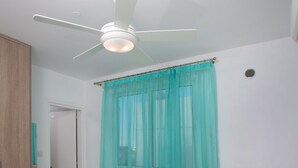 Quarto moderno com cama, ventilador de teto, cortinas verde-água e mesa de cabeceira com uma vela.