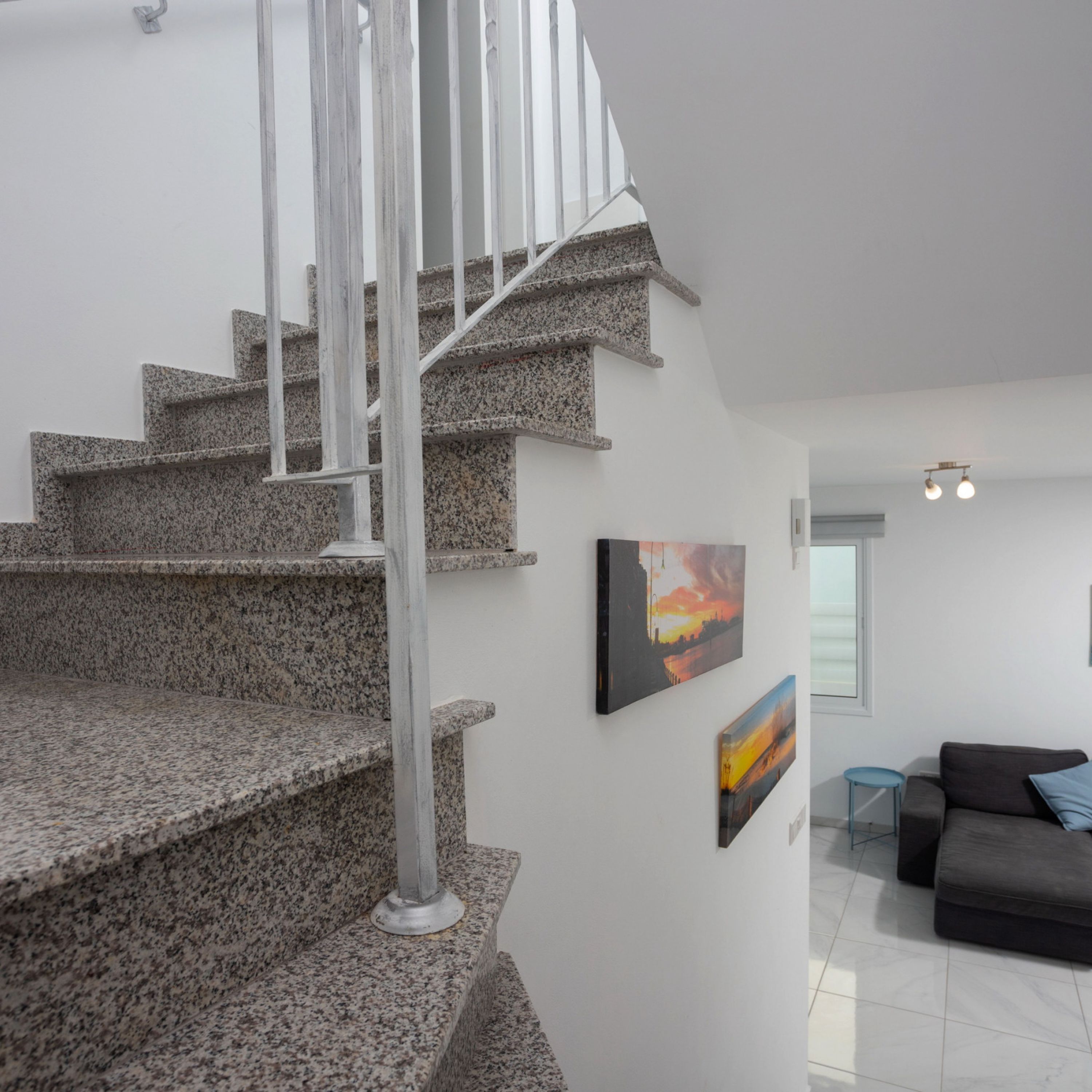 A modern interior with a granite staircase, white walls, and a grey sofa.