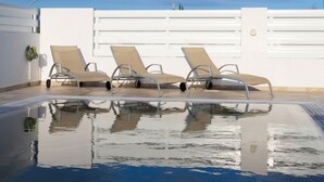 Uma área de piscina com três espreguiçadeiras e uma parede branca.