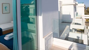Quarto de hotel moderno com uma grande porta de correr de vidro, varanda com guarda-corpos de vidro e vista para edifícios vizinhos.