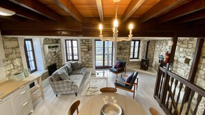A cozy living room with a stone wall, a fireplace, a sofa, a coffee table, and a dining table. - Leonys House in Dhoros (Dhoros)